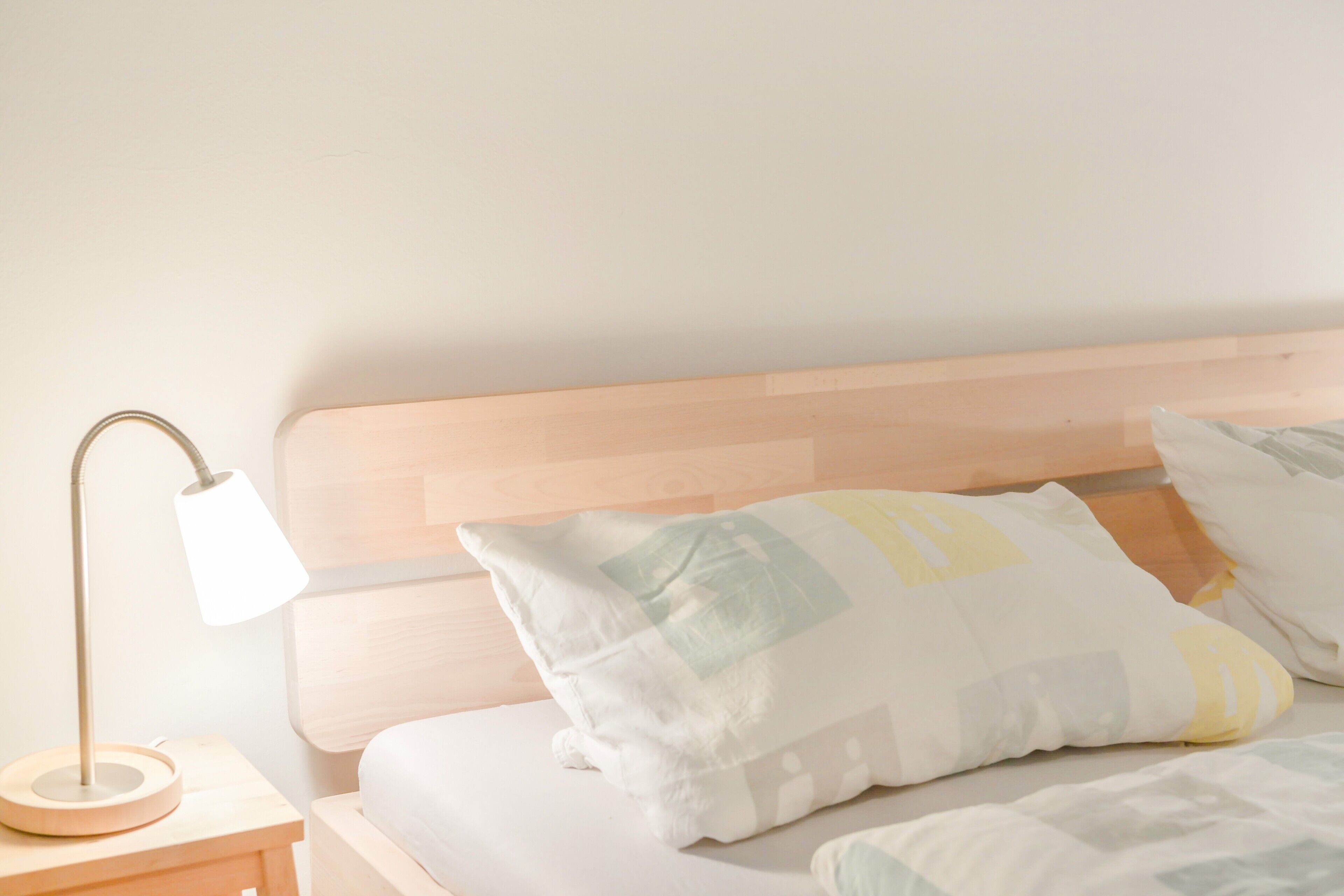 Een bed met een houten hoofdbord, een bedlampje en meerdere kussens.