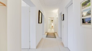 Un pasillo con paredes blancas, una puerta de madera y un cuadro enmarcado a la derecha.