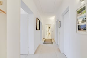 A hallway with white walls, a wooden door, and a framed picture on the right.