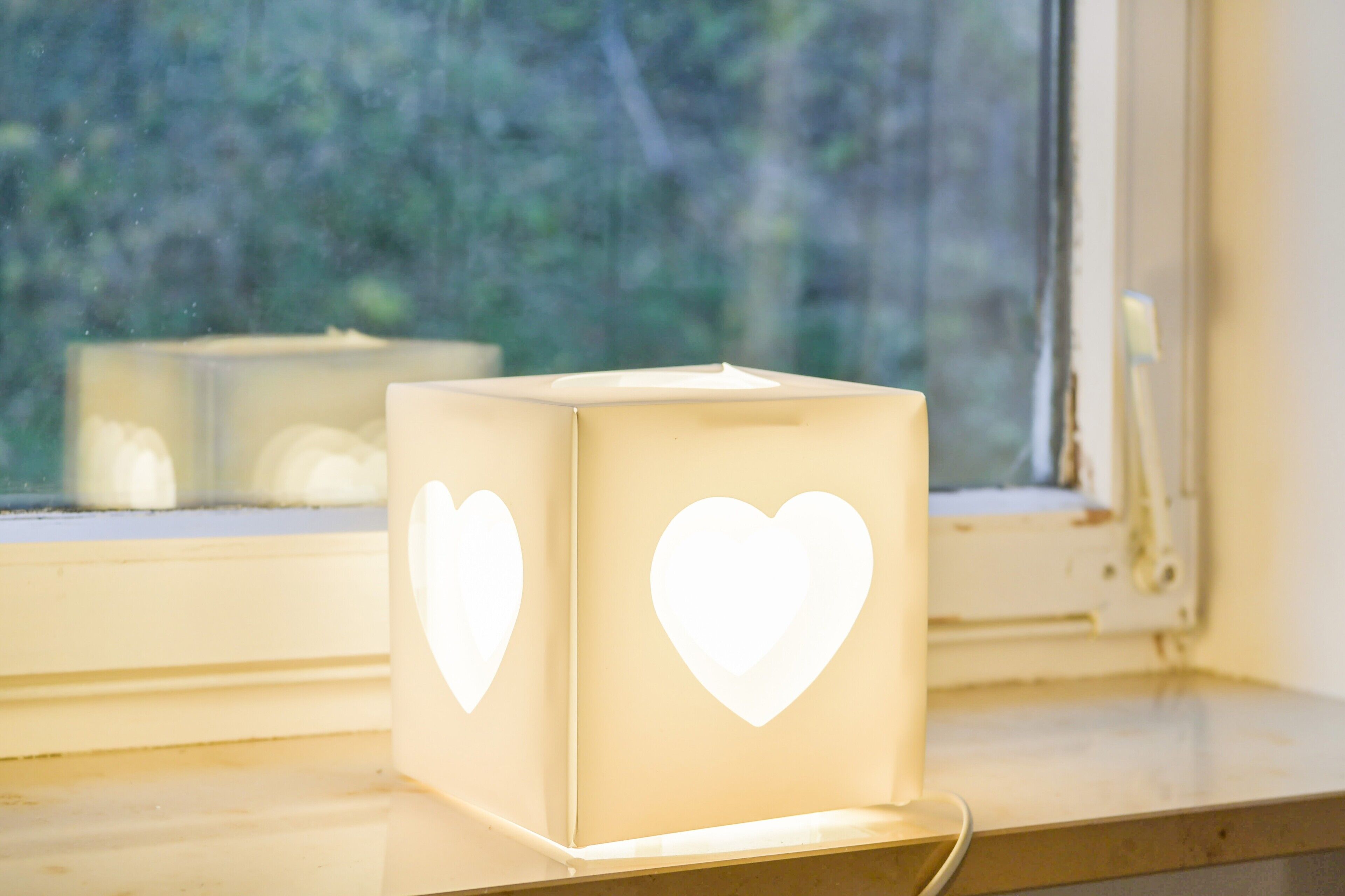 A cube-shaped box with heart cutouts on a windowsill.