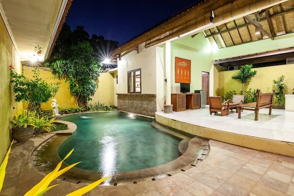 Una piscina con un borde de baldosas, rodeada de macetas con plantas y un banco de madera.