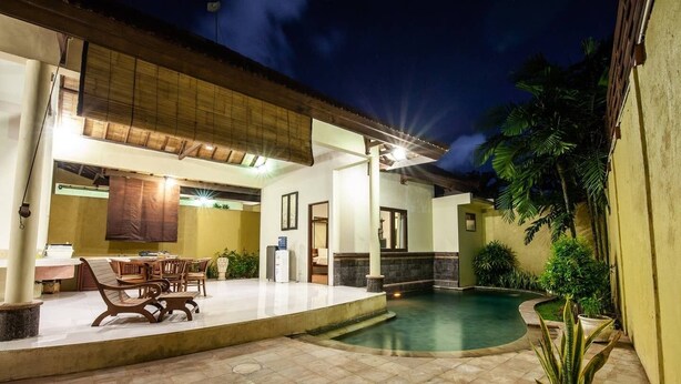 A well-lit outdoor area with a pool, a dining table with chairs, and a water dispenser. - 9-BR Private Pool Villa Walk to Seminyak Beach (Seminyak)