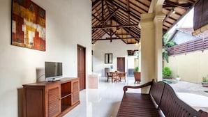 Amplia sala de estar con un banco de madera, un televisor sobre un mueble de madera y un comedor al fondo.