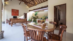 Un área de comedor con una mesa redonda de vidrio, sillas de madera, un banco de madera y un adorno rojo en la pared.