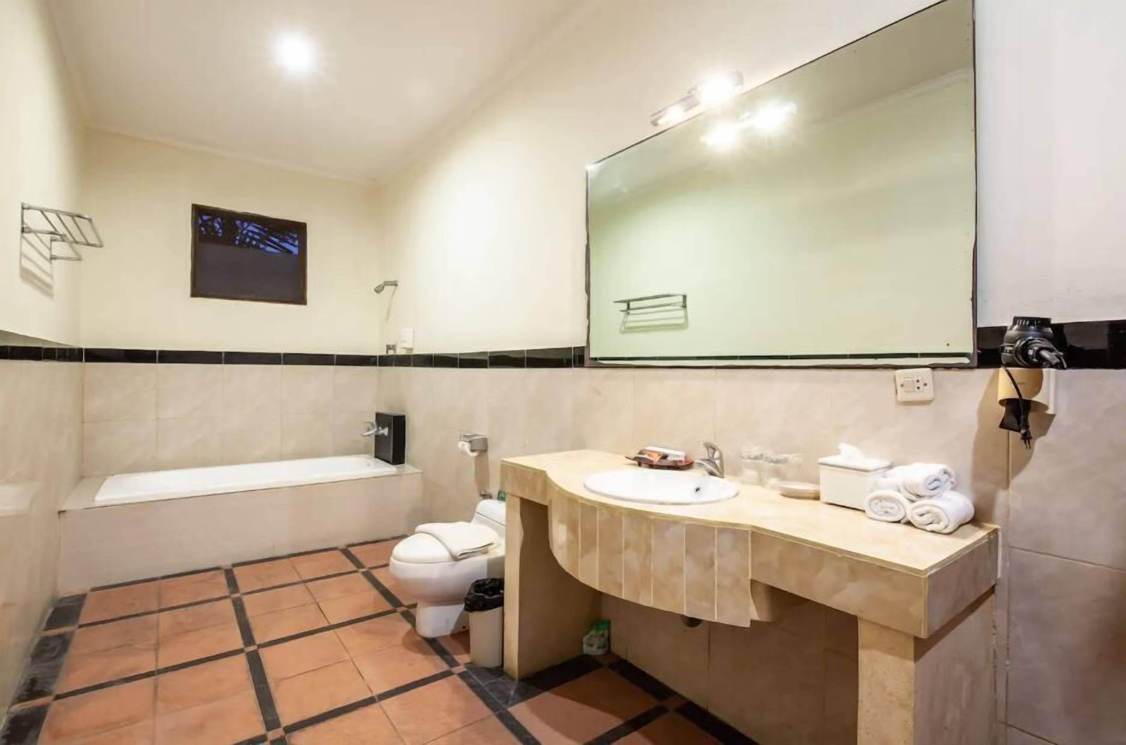 A bathroom with a bathtub, toilet, sink, and a large mirror.
