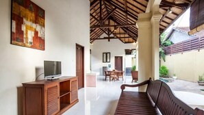 A spacious living area with a wooden bench, a TV on a wooden cabinet, and a dining area in the background. - PB - 7BR - V5 & V1 7BR Private Pool Villa, Walk to Seminyak Beach (Seminyak)