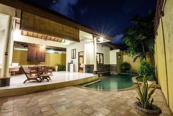 A well-lit outdoor area with a pool, a dining table, and chairs. - PB - 7BR - V5 & V1 7BR Private Pool Villa, Walk to Seminyak Beach (Seminyak)