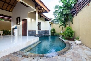 A swimming pool with a stone border, a covered patio, and a building with a tiled roof. - PB - 7BR - V5 & V1 7BR Private Pool Villa, Walk to Seminyak Beach (Seminyak)
