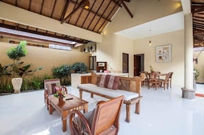 Un espacio interior amplio con techo alto, mobiliario de madera y plantas en macetas.