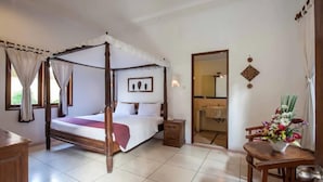 Ein Bett mit Baldachin und hölzernem Gestell, ein Nachttisch, ein kleiner Beistelltisch, ein Badezimmer, das durch eine offene Tür sichtbar ist, und ein Tisch mit einer Blumenkomposition.