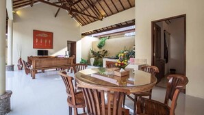 A dining area with a round glass table surrounded by wooden chairs, a wooden bench, and a red artwork on the wall. - PB - Villa 5 - 4BR · 4-BR Private Pool Villa Walk to Seminyak Beach (Seminyak)