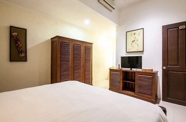 Une chambre à coucher avec un lit, une armoire en bois, une télévision et des œuvres d’art accrochées aux murs.