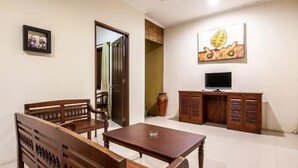A dining area with a wooden table and chairs, a television on a wooden cabinet, and a painting on the wall. - PB - Villa 5 - 4BR · 4-BR Private Pool Villa Walk to Seminyak Beach (Seminyak)