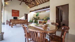 A spacious dining area with a round glass table and wooden chairs, a wooden bench, and a TV on the wall.