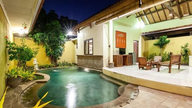 A swimming pool with a tiled deck, surrounded by potted plants and a wooden deck with outdoor furniture.