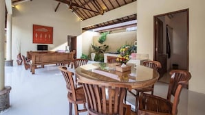 Un vaste espace dédié à la salle à manger, avec une table ronde en verre et des chaises en bois, un banc en bois et une œuvre d’art rouge accrochée au mur.