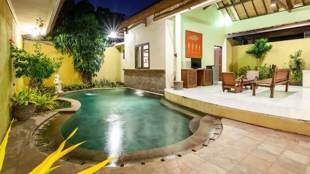 Une piscine dotée d’une terrasse carrelée, entourée de plantes en pot et agrémentée d’un espace de détente couvert, avec des meubles en bois.