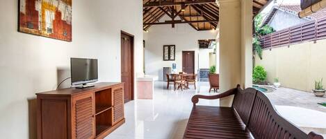 Una habitación amplia con un banco de madera, un televisor sobre un mueble y un comedor con sillas y una mesa.