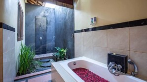 Ein Badezimmer mit einer Badewanne, gefüllt mit roten Kieselsteinen, einer Duschkabine und einer gefliesten Wand mit einem schwarz-beigen Muster.
