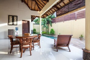 A spacious indoor area with a dining table and chairs, a water dispenser, and a door. - PB - Villa 2 - 2BR · 2-BR Private Pool Villa Walk to Seminyak Beach (Seminyak)