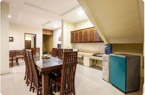 A dining area with a table and chairs, a kitchen with cabinets, a refrigerator, and a water dispenser.
