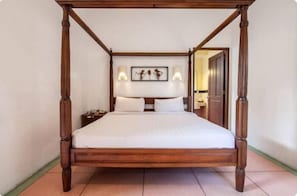 A four-poster bed with a wooden frame, white bedding, and wall-mounted sconces.