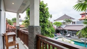 A balcony with a pool view, wooden furniture, and a stone pillar. - SMV - 3BedGRDN - V1 · 3BR Garden Villa Walk to Beach N Shops Legian (Legian)
