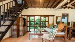 A spacious living area with a wooden staircase, a sofa with cushions, a wicker chair, and a coffee table with a vase of flowers. - SMV- 2BedGRDN - V6 · 2BR Garden Villa Walk to shops and Beach Legian (Legian)