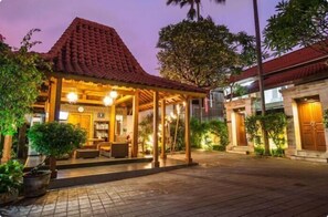 A well-lit outdoor area with a covered seating area, a stone building, and lush greenery.