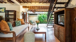 A spacious living area with a wooden ceiling, a sofa with cushions, a coffee table, and a television on a wooden cabinet. - SMV- 2BedGRDN - V7 · 2BR Garden Villa Walk to shops and Beach Legian (Legian)