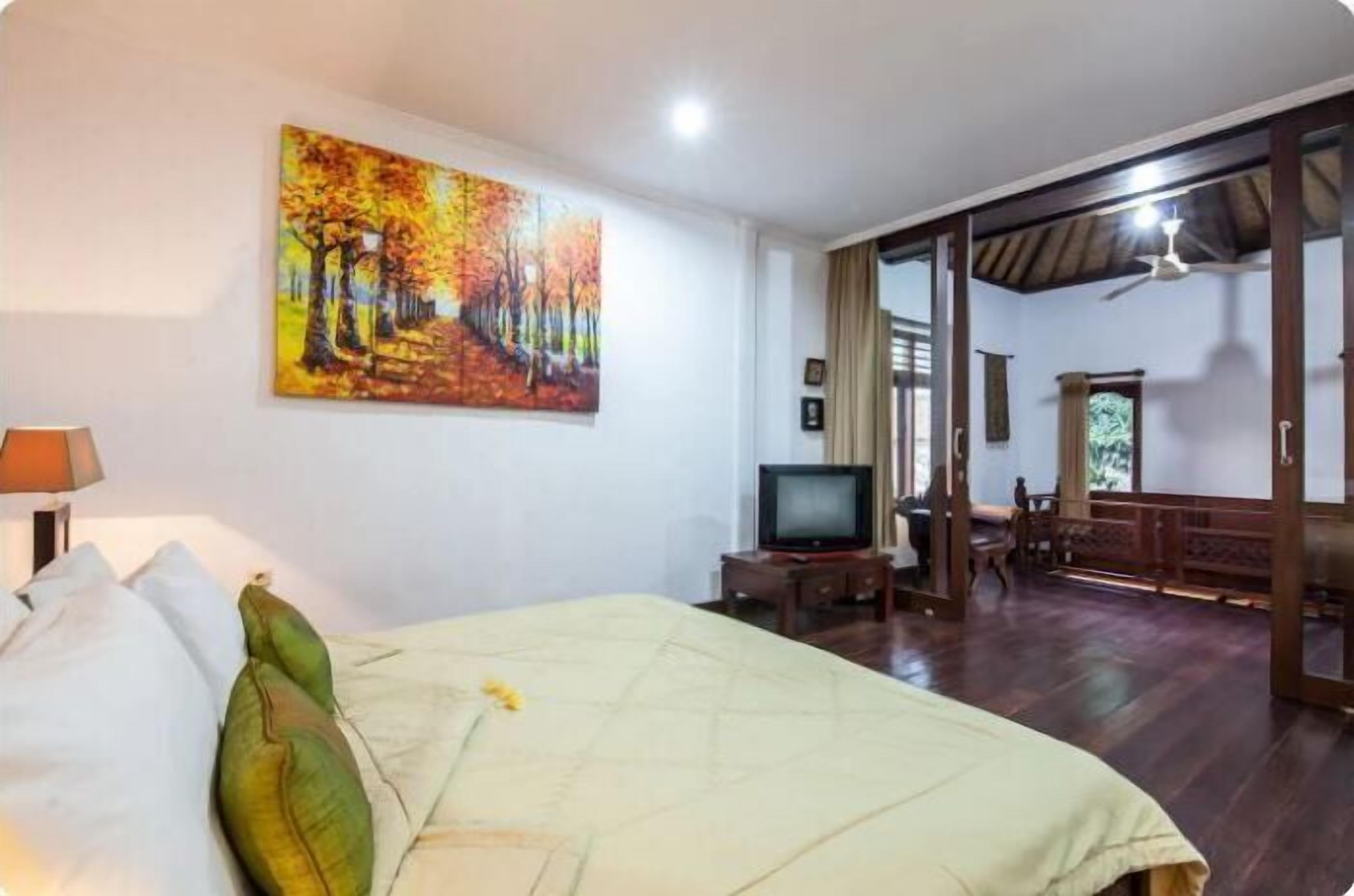 A hotel room with a bed, a television, a painting on the wall, and a view of the outside.
