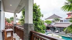 A balcony with wooden chairs, a stone pillar, and a view of a swimming pool and neighboring houses.