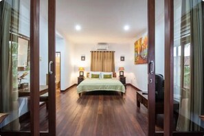 Une chambre avec un grand lit, un plancher en bois et une fenêtre avec des rideaux.