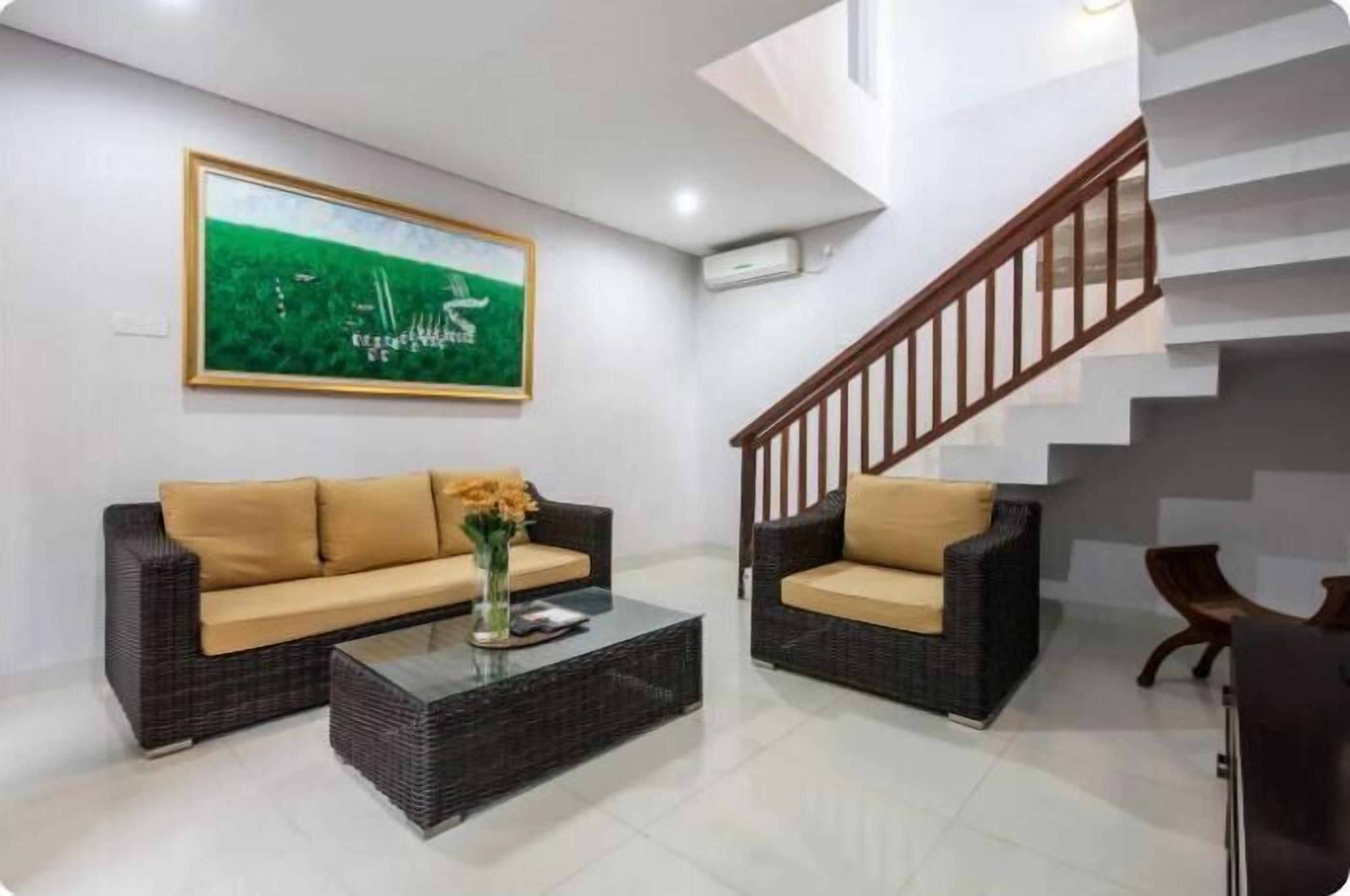 Una sala de estar moderna con dos sofás de mimbre, una mesa de centro de vidrio y una escalera con barandillas de madera.