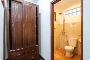 A wooden wardrobe with multiple drawers and a bathroom with a toilet, shower, and tiled walls.