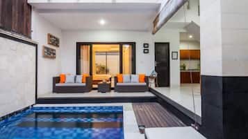 A modern outdoor living area with a pool, seating, and a view of the interior.