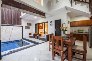 Un amplio salón con piscina, un comedor con mobiliario de madera y una cocina con armarios de madera.