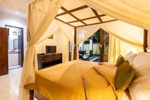 A bedroom with a canopy bed, a wooden headboard, a bedside table, and a view of the outside.