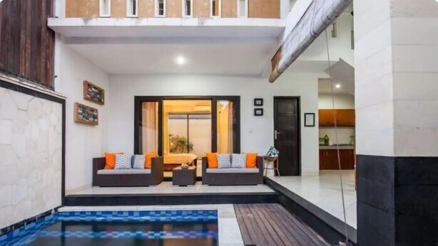 Un espace de vie moderne avec une piscine, deux canapés dotés de coussins et une porte-fenêtre coulissante donnant sur une cuisine.