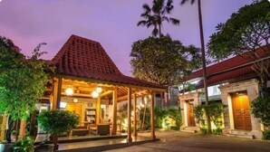 Un espace extérieur accueillant et bien éclairé, agrémenté d’un gazebo en bois, de plantes en pot et d’un bâtiment doté d’un toit en tuiles.