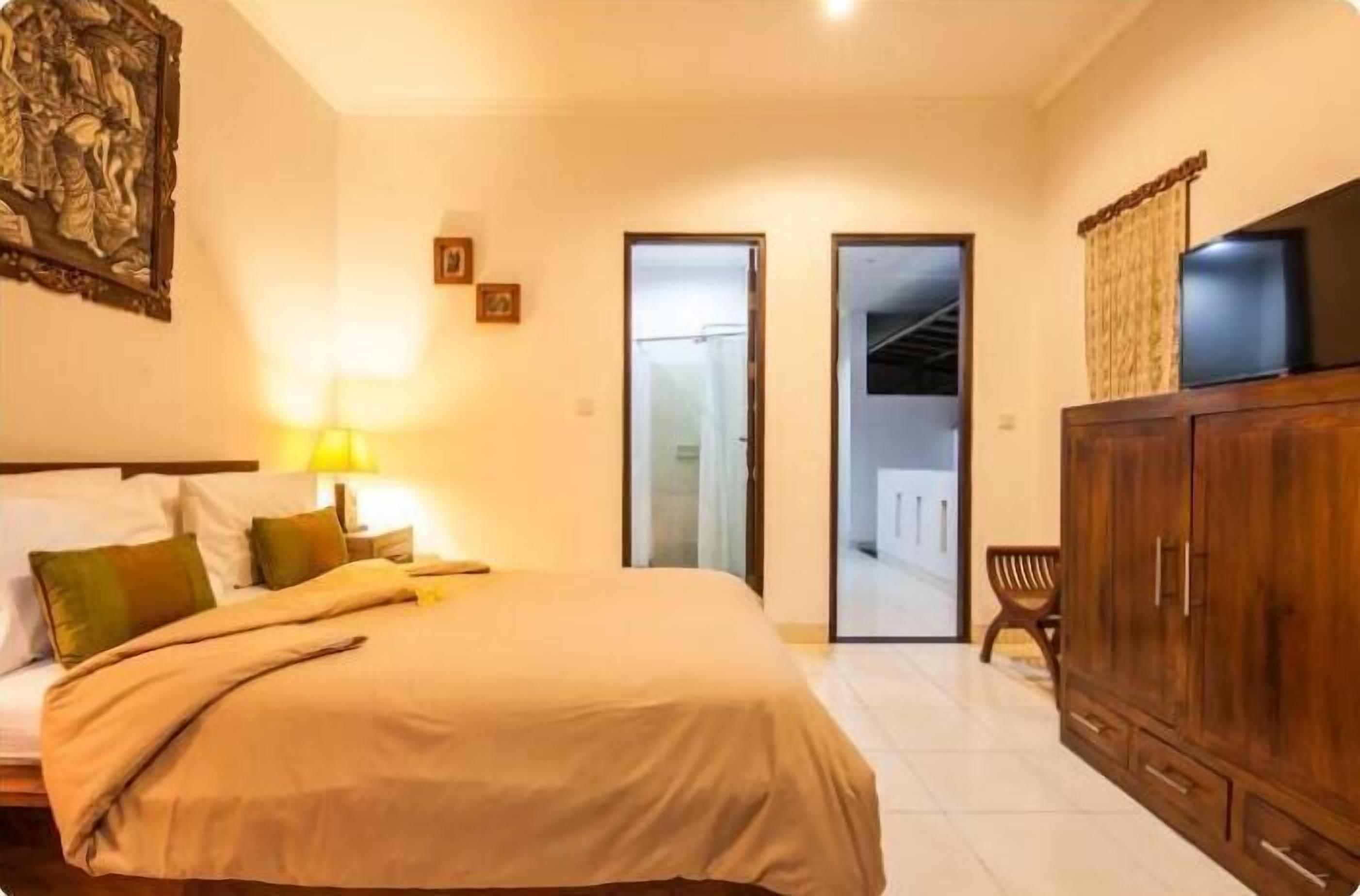 A hotel room with a bed, a wooden wardrobe, a television on top, and a door leading to a balcony.
