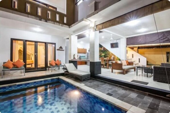 A modern hotel interior with a swimming pool, lounge areas, and a staircase leading to upper floors.