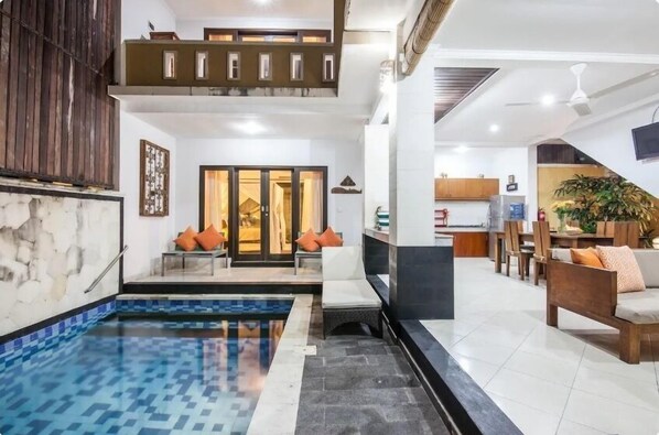 A modern living area with a pool, a staircase, and a dining area.
