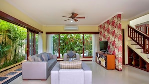 A spacious living room with a sofa set, a television, and a staircase. - Samudra · 3BR Luxury Private Pool Villa Bali (Kerobokan)
