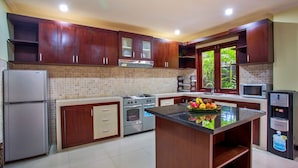 A modern kitchen with wooden cabinets, a central island, a refrigerator, stove, microwave, and a sink. - Samudra · 3BR Luxury Private Pool Villa Bali (Kerobokan)