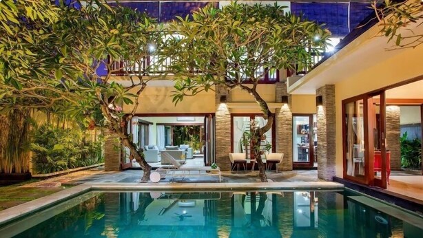 A swimming pool with a reflection of trees and a patio area with outdoor furniture. - Samudra · 6BR Luxury Family Pool Villa Umalas Bali (Kerobokan)