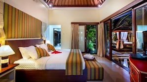 A bedroom with a large bed, a nightstand, a dresser, and a view of a lush garden through a glass door. - Samudra · 6BR Luxury Family Pool Villa Umalas Bali (Kerobokan)