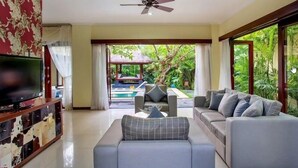 Una sala de estar con sofá, televisor y vistas a una piscina y jardín.