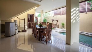 A spacious indoor area with a dining table and chairs, a small refrigerator, and a pool area with a view of the outdoors.