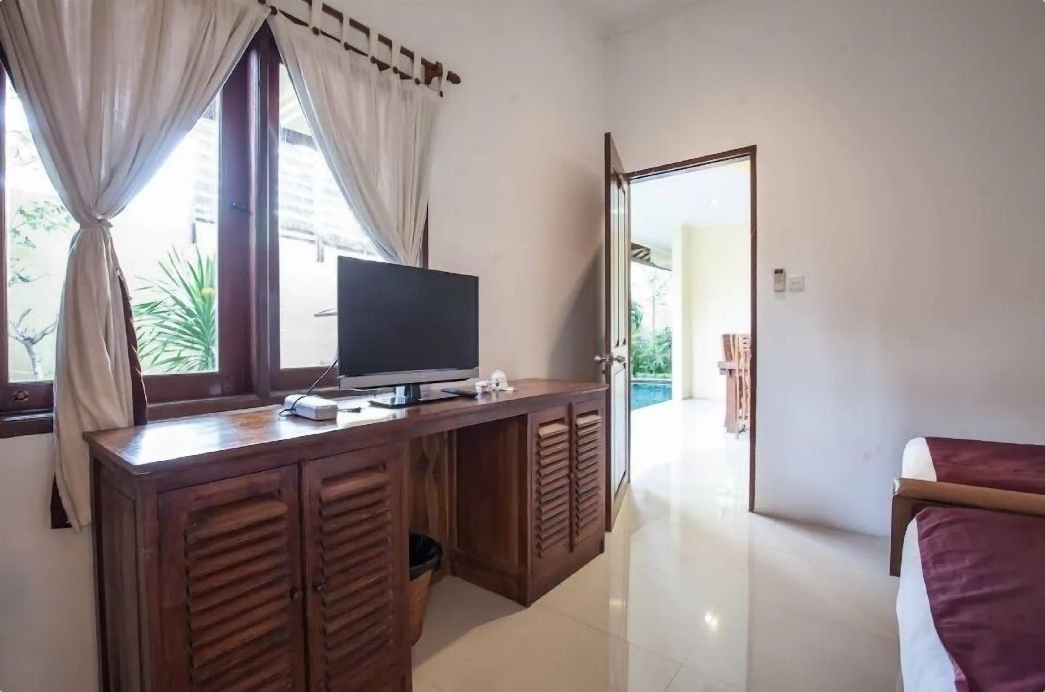 A room with a wooden desk, a television, and a bed.